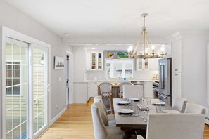 A modern kitchen with white cabinets, a dining area with a wooden table and chairs, and a chandelier.