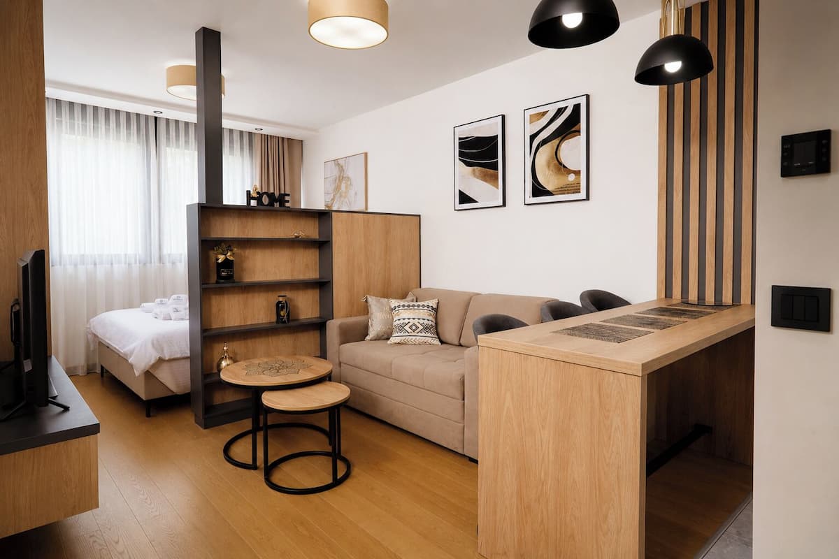 A modern hotel room with a bed, sofa, dining area, and artwork on the walls.