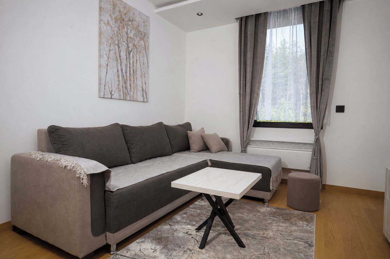 A modern living room with a grey sofa, a white coffee table, and a window with curtains.