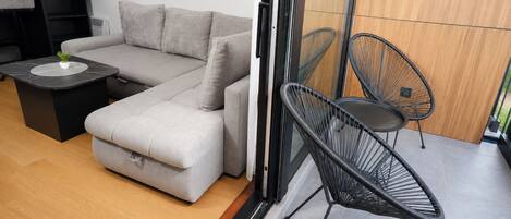 Un espacio habitable moderno con un sofá gris, una mesita con una planta y dos sillas negras.