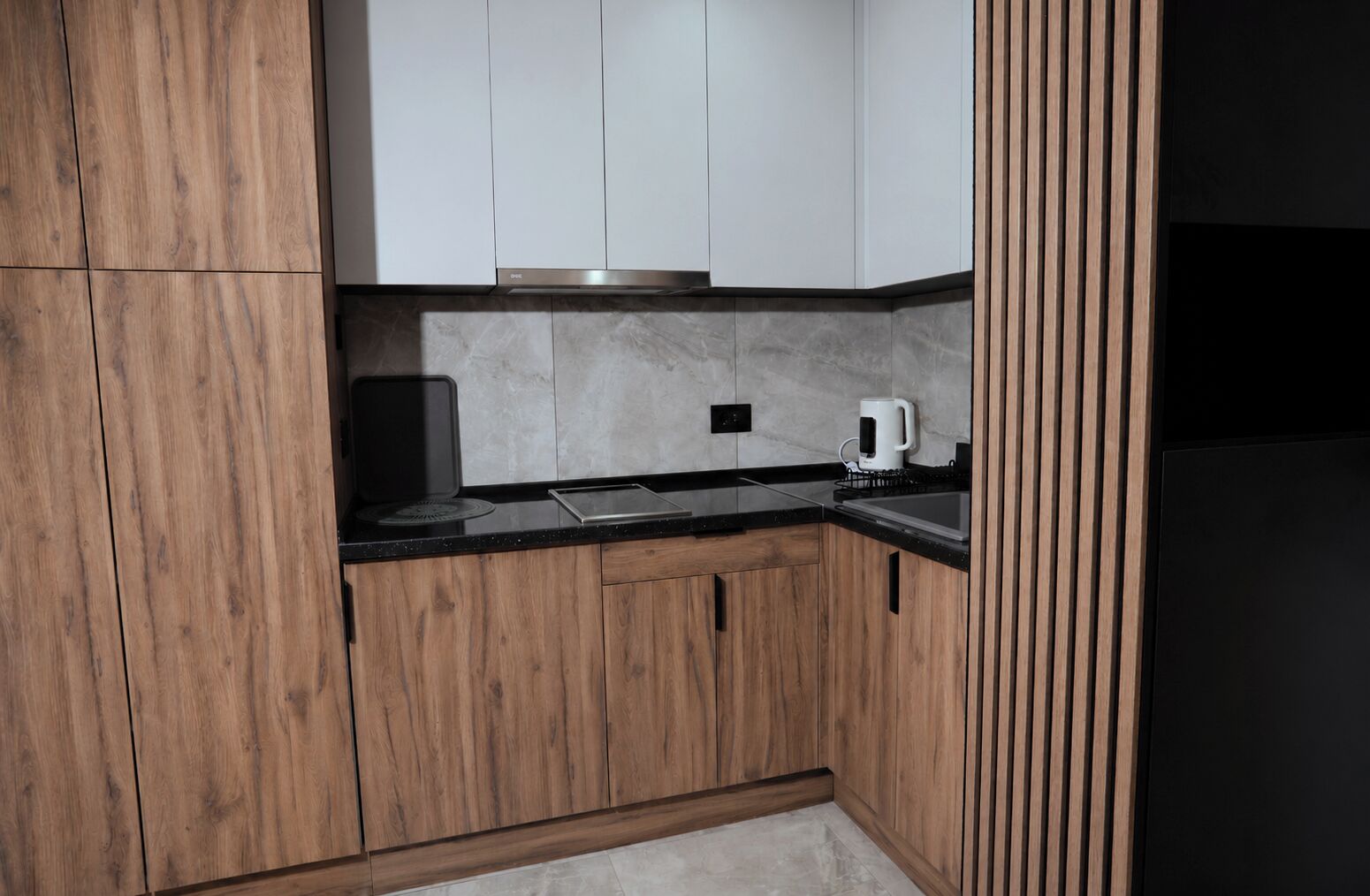A kitchen with wooden cabinets, a black countertop, a white coffee maker, and a stainless steel range hood.