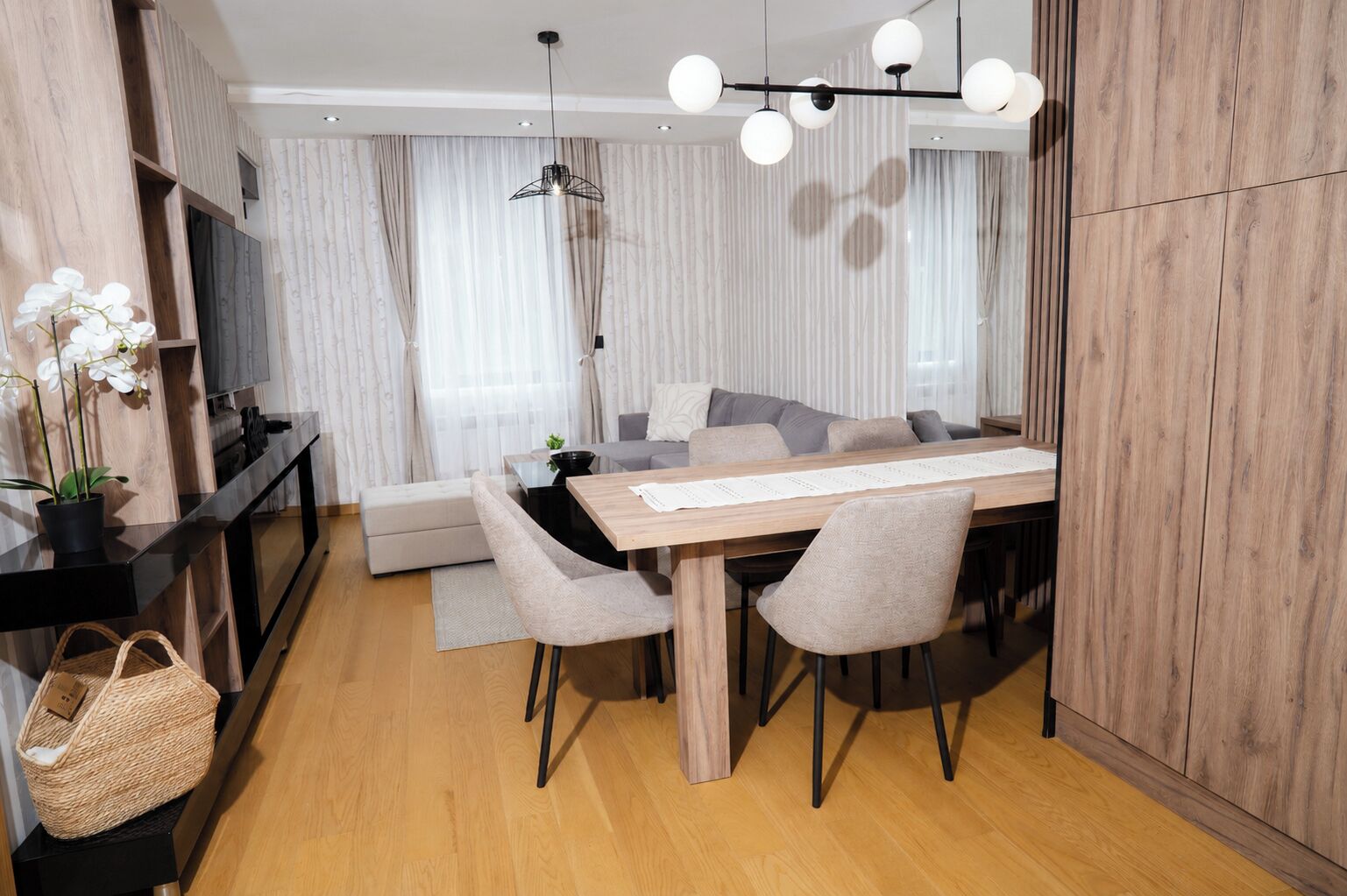 A modern dining area with a wooden table, grey upholstered chairs, and a hanging light fixture.