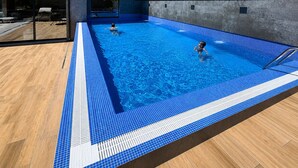 Una piscina con bordes de azulejos, una terraza de madera y un edificio con balcones.