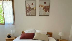 Ein Schlafzimmer mit Bett, Kissen, einem Nachttisch, einer Lampe und zwei Wandbildern.