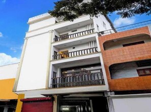 A multi-story building with balconies, a red shuttered entrance, and a clear blue sky. - Collection O Murugan Temple Ooty (Ootacamund)