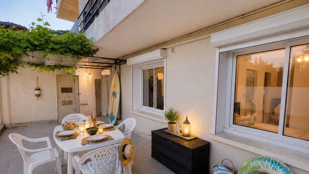 Un patio con mesa lista para comer, asientos exteriores y una tabla de surf apoyada en la pared.