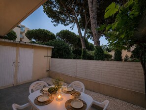 Een terras buiten met een eettafel, omringd door witte stoelen, een kaars en een schaal fruit.