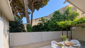 Un patio al aire libre con una mesa preparada para comer, rodeado de sillas de plástico blanco y un bajo muro de piedra.