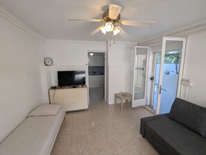 Een woonkamer met een televisie, bank en plafondventilator.