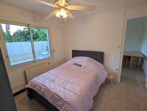 Een slaapkamer met een bed, een plafondventilator, een raam en uitzicht op buiten.