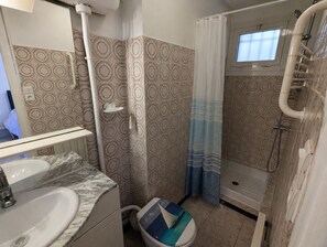 Een badkamer met een wastafel, toilet, douche en een raam.