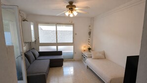 Una habitación compacta con sofá, cama, ventilador de techo, televisor y ventana con vidrio esmerilado.