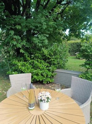 A round wooden table with wicker chairs, a vase with flowers, and a bottle. - Beautiful apartment directly at the Kurwald (Bad Lippspringe)