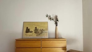Eine Holzkommode mit Schubladen, ein gerahmtes Bild darauf und eine Vase mit getrockneten Blumen.