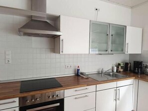 A kitchen with white cabinets, a stainless steel range hood, a double sink, and a wooden countertop. - Beautiful apartment directly at the Kurwald (Bad Lippspringe)