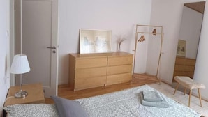 Ein Schlafzimmer mit einem Holzkoffer, einem Bett mit gemustertem Überwurf, einer Nachttischlampe und einem Spiegel.