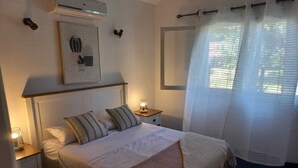 A bedroom with a bed, bedside tables, a wall-mounted air conditioner, a framed picture, and sheer curtains. - Tile villa in residential neighborhood, 3 minutes from the beach. (Punta del Este)