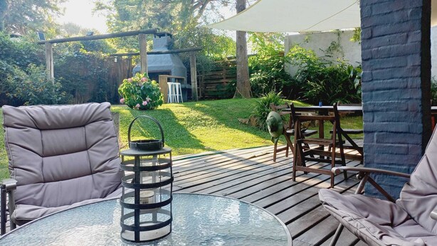 An outdoor patio with a round glass table, cushioned chairs, a lantern, and a pergola. - Tile villa in residential neighborhood, 3 minutes from the beach. (Punta del Este)