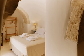 Ein Schlafzimmer mit einem Bett, einer Holzleiter, einem Nachttisch mit Lampe und einer Wand mit strukturierter Oberfläche.