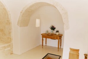 Ein Zimmer mit einer Steinwand, einem Holztisch mit einer Vase und Teekannen sowie einem kleinen Fenster.