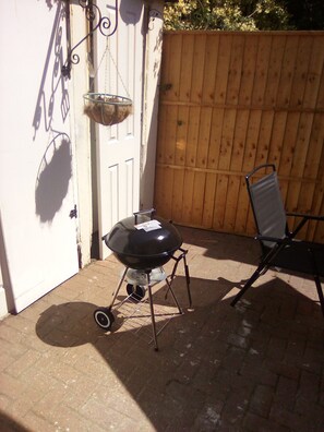 Ein Grill mit Metallständer, ein Stuhl und ein Holzzaun in einem Hinterhof.