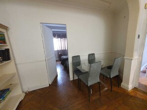 Ein Zimmer mit Esstisch, Stühlen, einem Bücherregal und einer Tür zu einem anderen Raum.