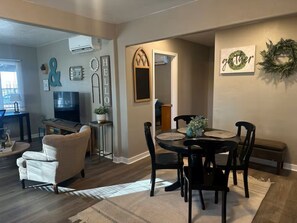 Ein Wohnzimmer mit Fernseher, Sitzgelegenheiten und einem Essbereich mit Tisch und Stühlen.