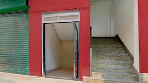 Un edificio con fachada roja, un persiano verde cerrado y una escalera que conduce a un piso superior.