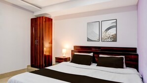 Un dormitorio con cama, armario, mesita de noche con lámpara y dos obras de arte colgadas en la pared.