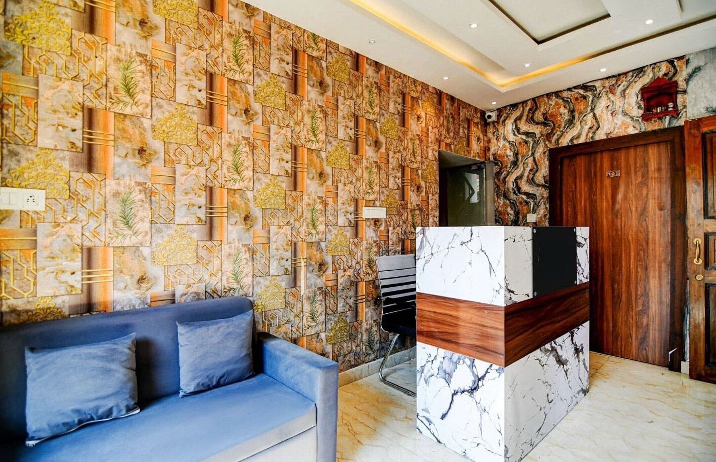 Un área de recepción con un muro estampado, un sofá azul, una columna de mármol y una puerta de madera.
