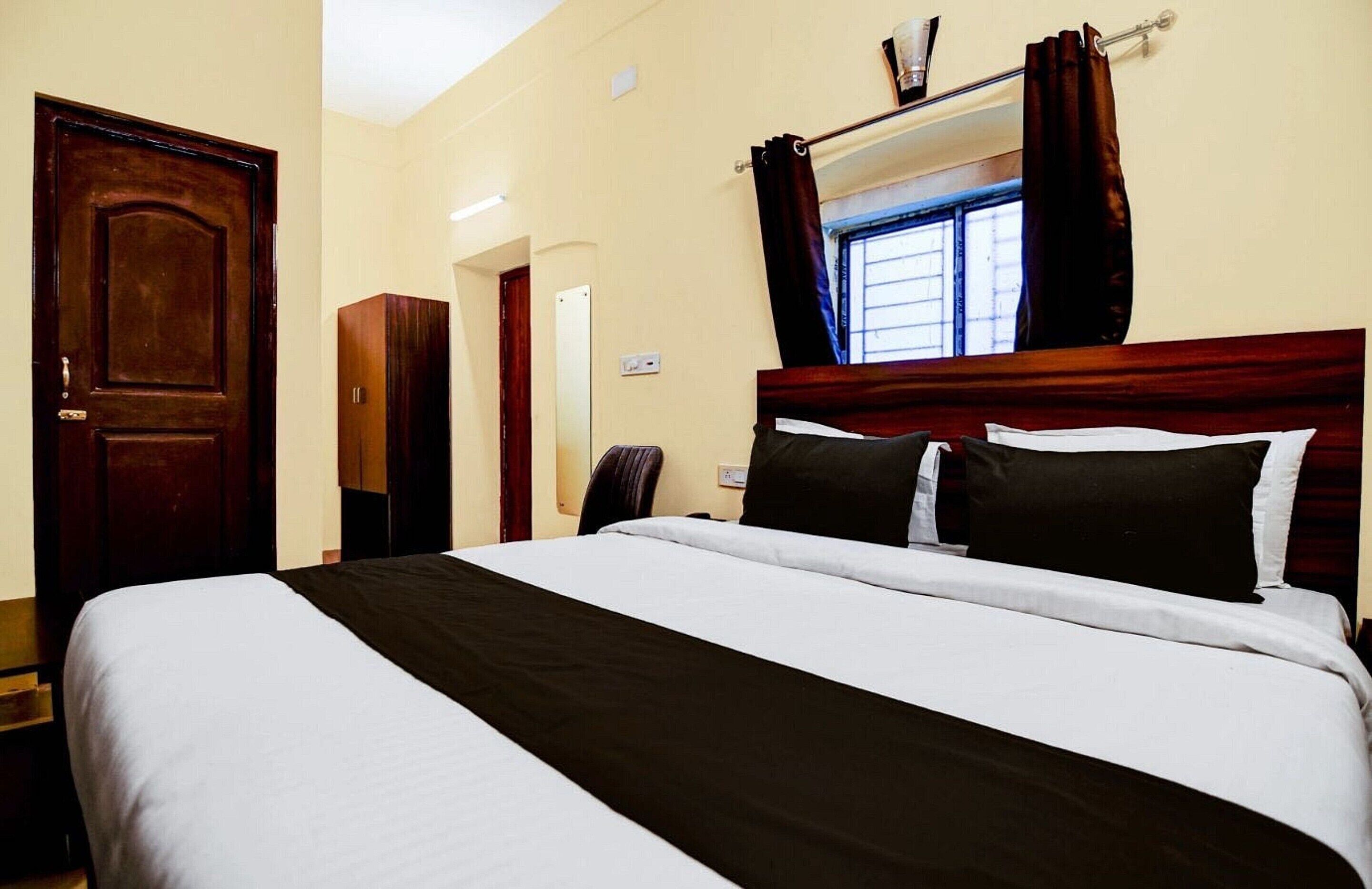 A hotel room with a bed, a wardrobe, a mirror, a window with curtains, and a door.