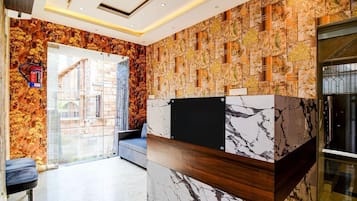 Un área de recepción con un mostrador de mármol, un muro decorado y una puerta de vidrio que da al exterior.