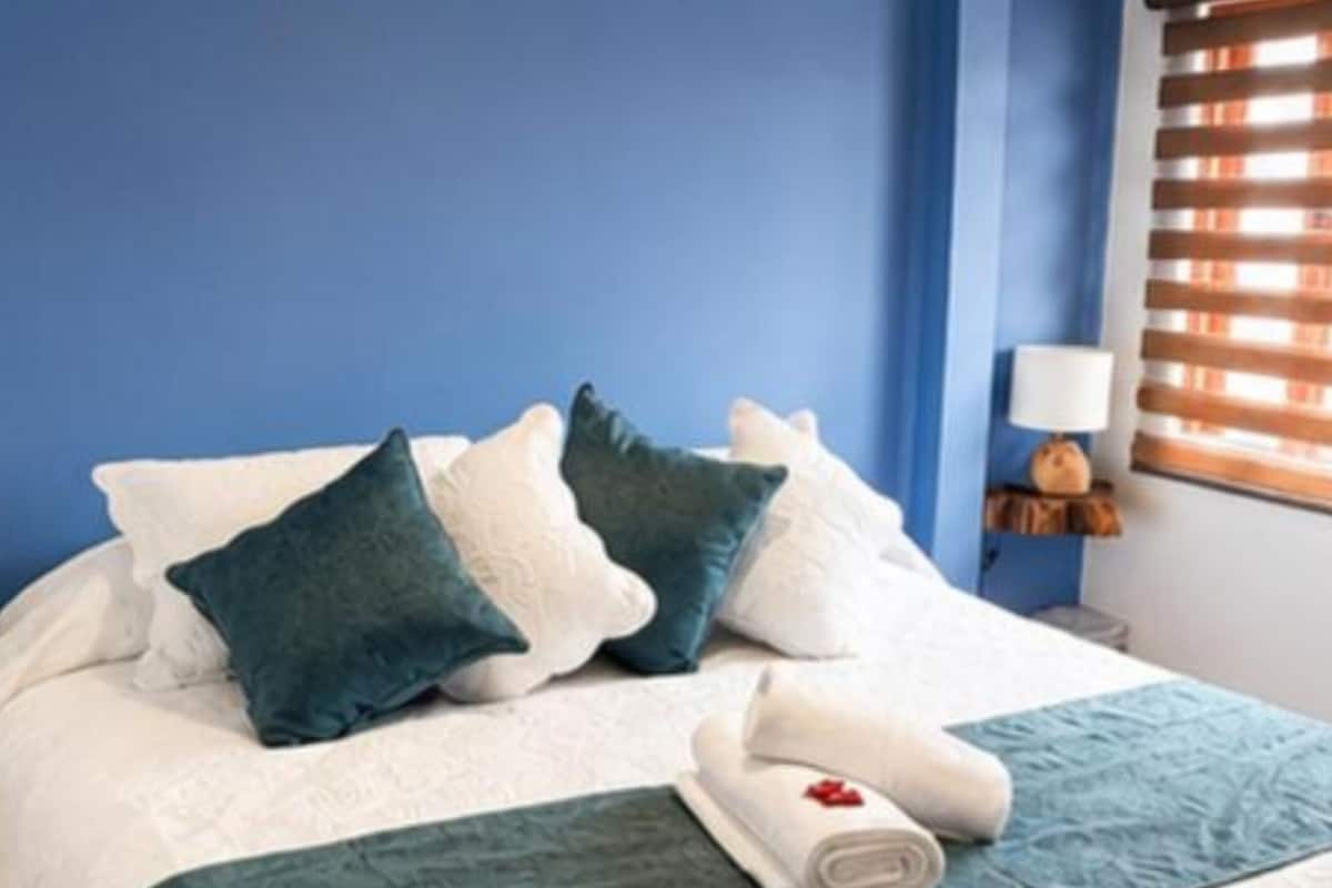 A neatly made bed with pillows, a rolled towel, and a bedside table with a lamp.