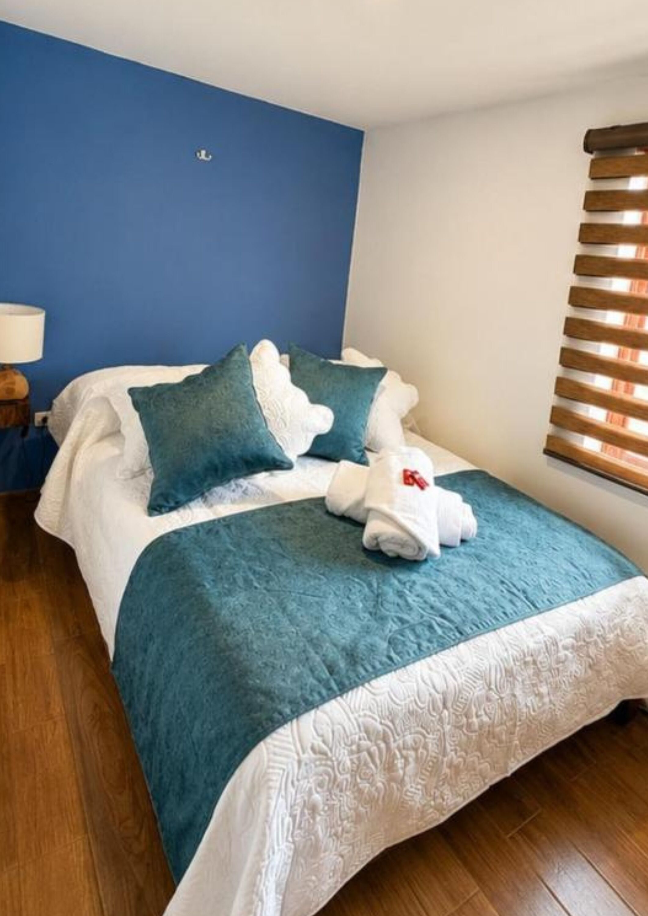 A neatly made bed with a blue and white duvet, two pillows, and a set of white towels.