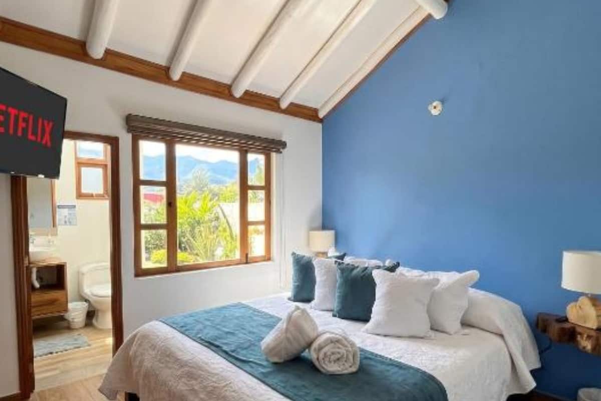 A bedroom with a bed, a TV, a window, and a view of the outdoors.
