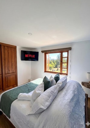 A bedroom with a bed, a TV mounted on the wall, a window with a view, and a wooden wardrobe.