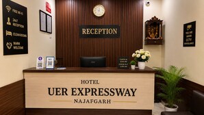 Et hotelreceptionsskrank med et ur, et skilt der angiver receptionens åbningstider, samt et skilt med teksten 'Hotel Uer Expressway Najafgarh'.