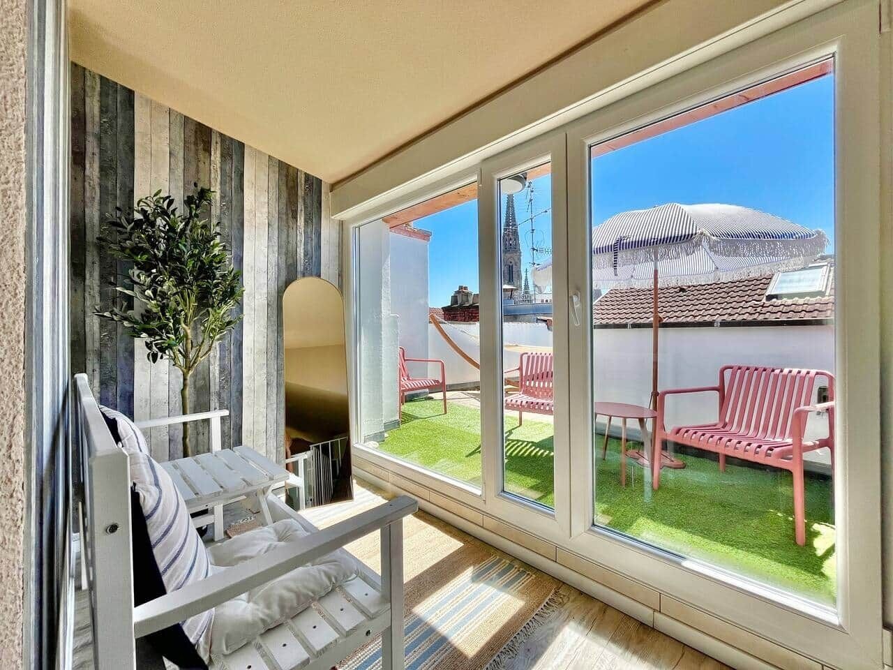 En balkon med en hvid stol, en plantekasse og udsigt til en rød bænk og parasol.