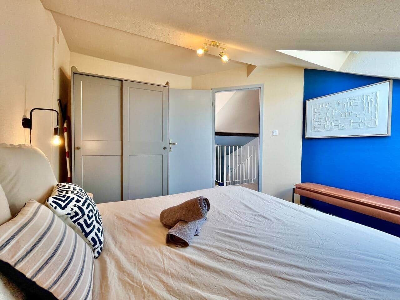 Een slaapkamer met een bed, een bankje, een kledingkast, een trap en een wand met een ontwerp.