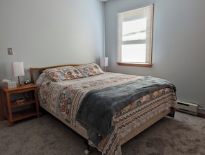 A bedroom with a bed, nightstand, lamp, and window.
