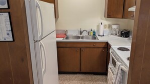 Cocina compacta con armarios de madera, un refrigerador blanco, un lavamanos con escurreplatos y una cafetera.