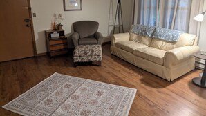 Una sala de estar con sofá, sillón, otomanas, lámpara de pie y alfombra.