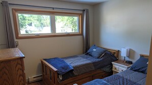 Un dormitorio con dos camas de madera, una mesita de noche con lámpara, un aparador y una ventana con cortinas.
