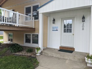 A two-story building with a white exterior, a balcony with a railing, and a front door with a mailbox.
