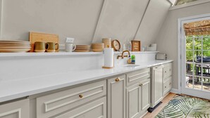 A kitchen with a white countertop, wooden utensils, a clock, and a window with a view of greenery.