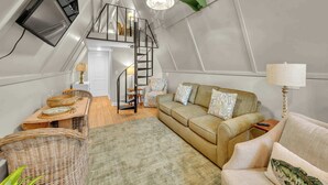 A loft-style room with a sofa, a dining table, and a staircase.