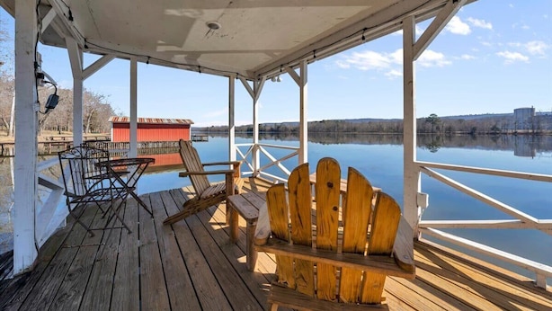 A wooden deck with a covered area, a red building in the background, and a calm body of water.