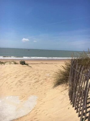 Ein sandiger Strand mit Holzzaun und Blick auf den Ozean.