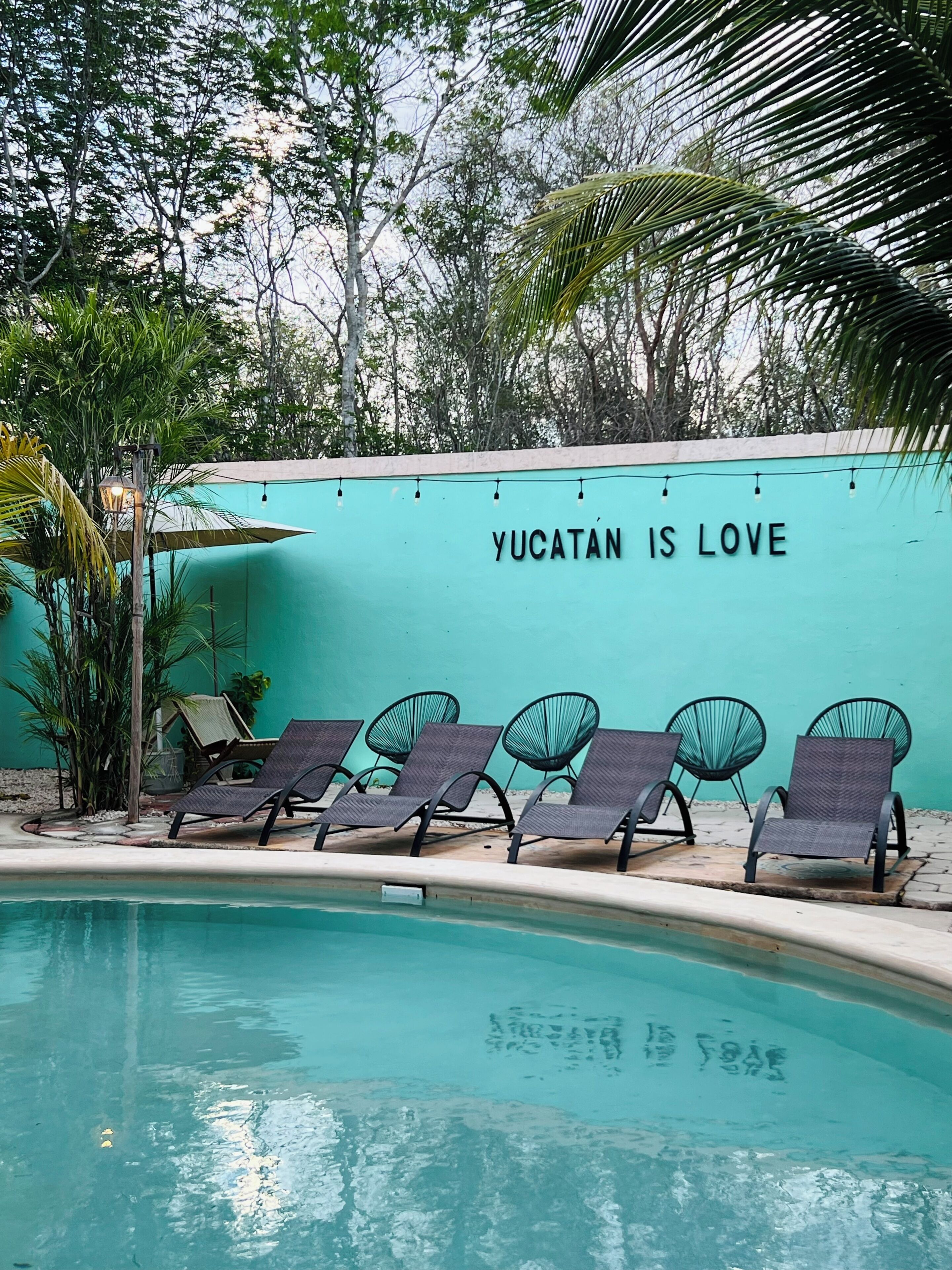 A poolside area with lounge chairs and a wall with the text 'Yucatan is love'.