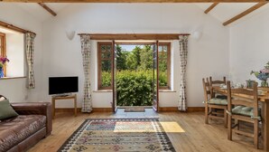 Una habitación con techo de madera, un sofá de cuero marrón, una mesa de comedor con sillas, un televisor sobre un mueble bajo y una alfombra estampada.